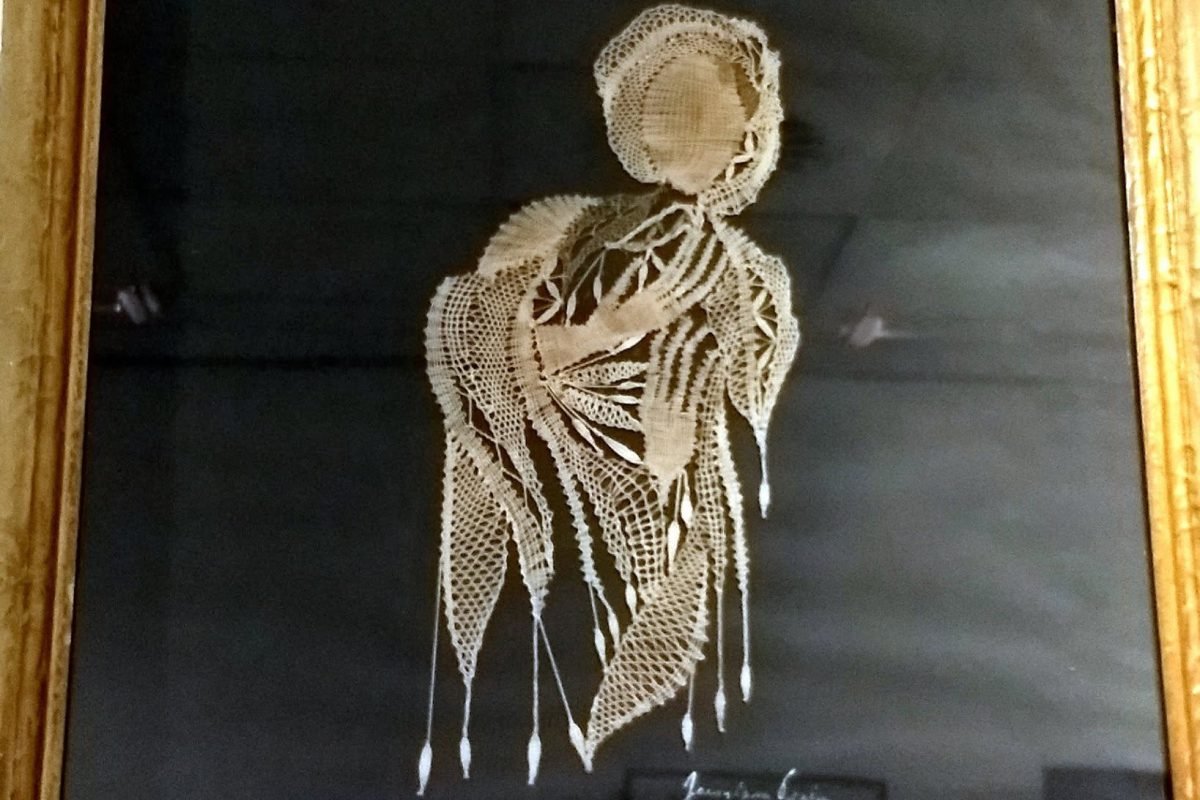 Gerahmtes Klöppelbild einer Frauengestalt auf schwarzem Grund