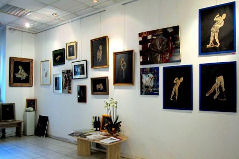 Galerieecke mit gerahmten Klöppelbildern an weißen Wänden