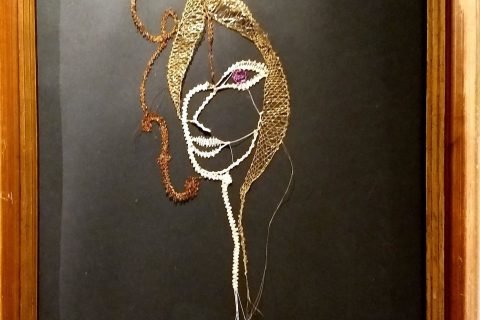 Gerahmtes Klöppelbild eines Frauenprofils mit Goldfäden auf schwarzem Grund