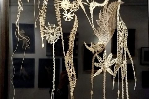 Gerahmtes Klöppelbild mit langen herabhängenden Fäden und Blüten